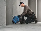 Một người đàn ông mặc đồ bảo hộ đang dùng dụng cụ điện để cắt một rãnh trên bê tông.