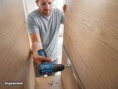 Một người đàn ông đeo thiết bị bảo hộ đang sử dụng máy khoan không dây để lắp đặt ray trượt ngăn kéo trong tủ gỗ.