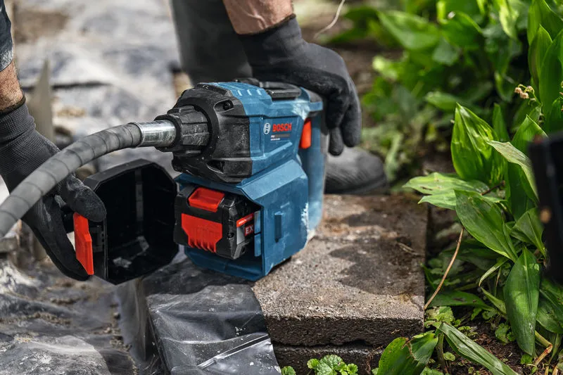 Một người đàn ông đeo thiết bị bảo hộ đang vận hành dụng cụ điện trên một viên đá trong vườn.