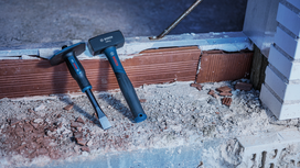 Búa và đục xây đặt trên bề mặt gạch phủ đầy bụi tại một công trường xây dựng.