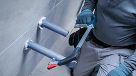 Một người đàn ông mặc đồ bảo hộ đang dùng cưa sắt cắt một đường ống.