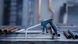 Một chiếc cưa sắt được đặt trên bàn làm việc bằng kim loại gần các đường ống đồng trong một môi trường công nghiệp.