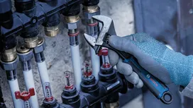 Một người đàn ông mặc đồ bảo hộ đang siết chặt một khớp nối bằng cờ lê trên một cụm ống dẫn.