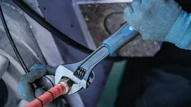 Một người đàn ông mặc đồ bảo hộ đang siết chặt khớp nối ống bằng cờ lê điều chỉnh.