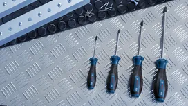 Bốn chiếc tua vít được sắp xếp trên một bề mặt kim loại bên cạnh các ốc vít và thanh kim loại.