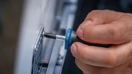 Một người đang dùng tua vít để siết chặt một con ốc trên một tấm kim loại.