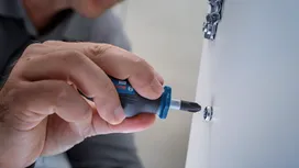 Một người dùng tua vít để vặn ốc vít vào một tấm bảng màu trắng.
