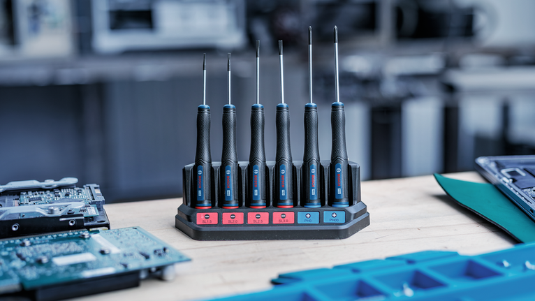 Bộ tua vít chính xác được đặt trong đế sạc trên bàn làm việc.
