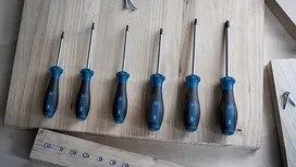 Sáu chiếc tua vít màu xanh và đen được sắp xếp theo kích cỡ trên một chiếc bàn làm việc bằng gỗ sáng màu.