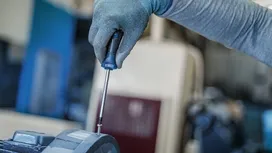 Một người đàn ông mặc đồ bảo hộ đang dùng tua vít siết chặt một con ốc.