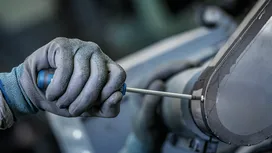 Người đàn ông mặc đồ bảo hộ dùng tua vít để siết chặt tấm vỏ máy.
