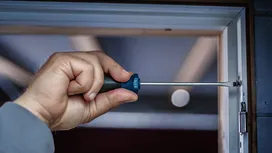 Một người đang dùng tua vít để siết chặt ốc vít trên khung cửa.