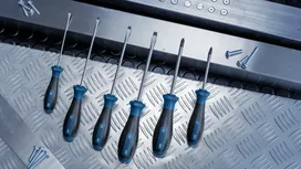 Một bộ tua vít được sắp xếp trên bề mặt kim loại bên cạnh những con ốc vít nằm rải rác.
