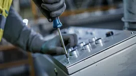 Một người đàn ông mặc đồ bảo hộ đang dùng tua vít siết chặt một con ốc trên bảng điều khiển.