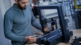 Một người đang lắp ráp khung máy in 3D trên bàn làm việc bằng tua vít.