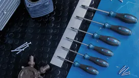 Sáu chiếc tua vít được sắp xếp theo kích cỡ trên một mặt bàn màu xanh lam, bên cạnh các bu lông kim loại.