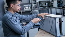 Một người đàn ông mặc đồ bảo hộ đang siết chặt một con ốc trên hộp điện bằng kim loại.