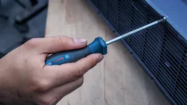 Một người đang dùng tua vít để siết chặt một con ốc trên ống thông gió bằng kim loại.
