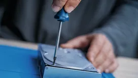 Người đang dùng tua vít để siết chặt một con ốc vít trong một thiết bị kim loại.