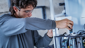 Một người đàn ông mặc đồ bảo hộ đang siết chặt một con ốc trên bảng điều khiển điện.