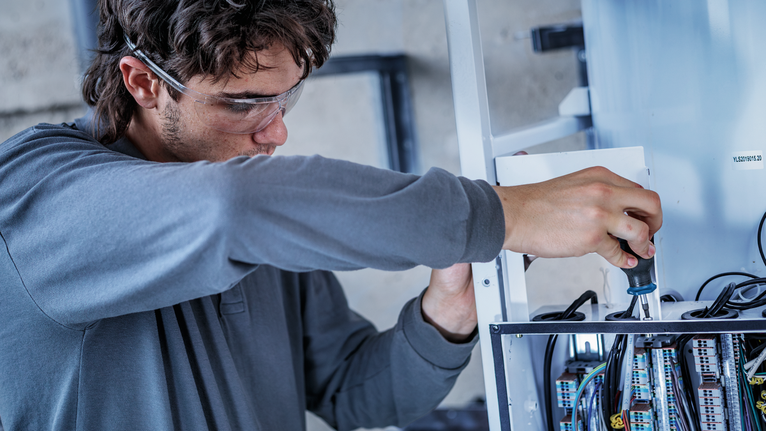 Một người đàn ông mặc đồ bảo hộ đang siết chặt một con ốc trên bảng điều khiển điện.