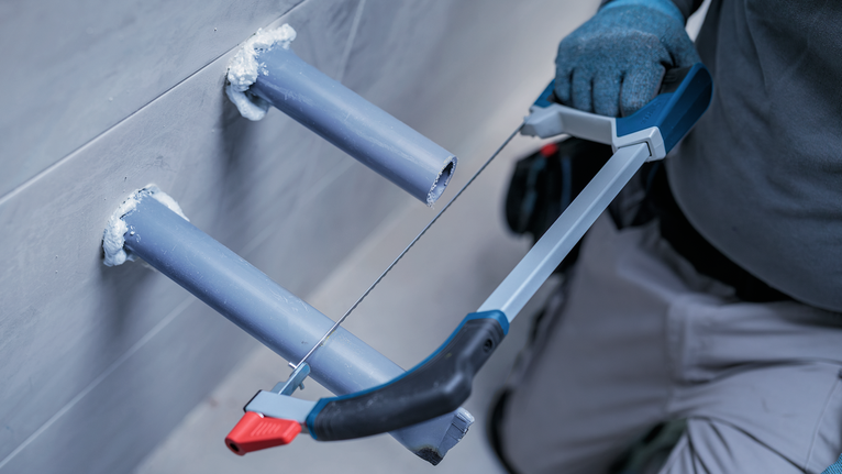 Một người đàn ông mặc đồ bảo hộ đang dùng cưa sắt cắt ống nhựa PVC.