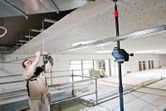 Một người mặc thiết bị an toàn đang căn chỉnh khung trần nhà bằng dụng cụ cân bằng laser.