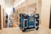 Bộ sạc radio trên bề mặt gỗ trong khu vực đang xây dựng với hai công nhân ở phía sau.