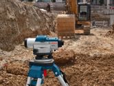 Máy cân bằng laser trên chân máy tại một công trường xây dựng gần máy xúc.