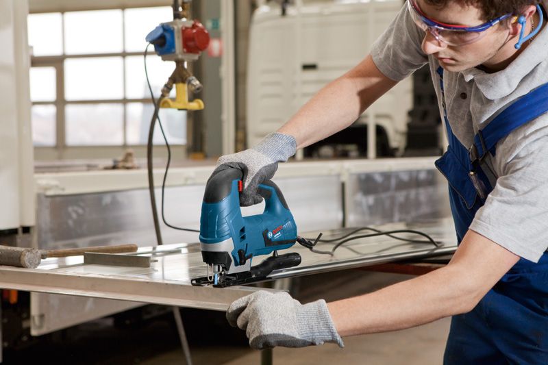 Một người mặc đồ bảo hộ đang sử dụng máy cưa lọng để cắt một tấm kim loại.