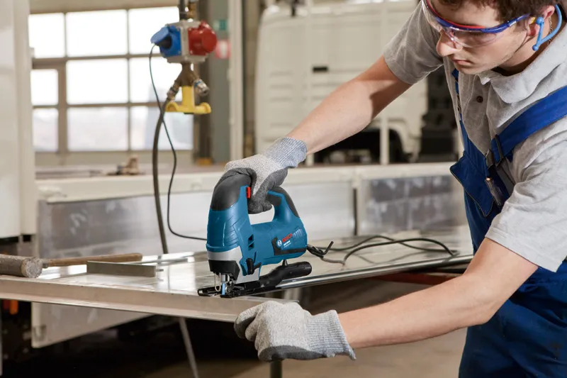 Một người mặc đồ bảo hộ đang sử dụng máy cưa lọng để cắt một tấm kim loại.