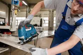 Một người mặc đồ bảo hộ đang điều khiển máy cưa lọng để cắt một tấm kim loại.