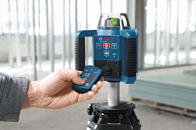 Một người đang vận hành thiết bị cân bằng laser đặt trên giá ba chân tại một công trường xây dựng.