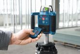 Một người đang vận hành thiết bị cân bằng laser đặt trên giá ba chân tại một công trường xây dựng.