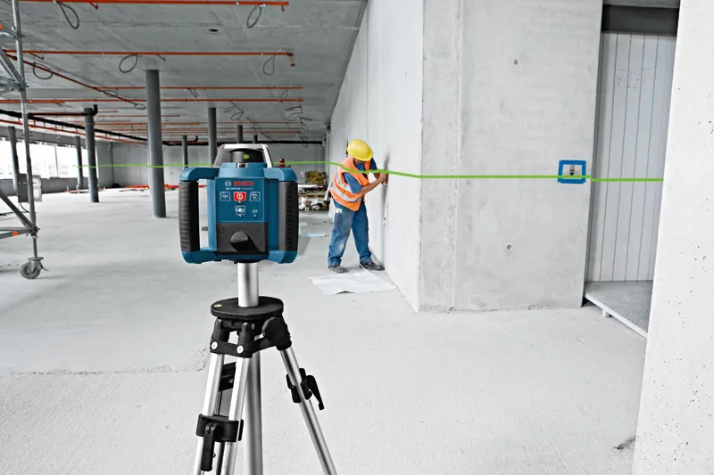 Một người mặc đồ bảo hộ đang dùng dụng cụ cân bằng laser màu xanh lá cây để đánh dấu vị trí trên tường.