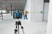 Một người mặc đồ bảo hộ đang dùng dụng cụ cân bằng laser màu xanh lá cây để đánh dấu vị trí trên tường.