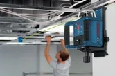 Máy cân bằng laser chiếu một đường màu xanh lá cây khi một người lắp đặt tấm trần nhà.