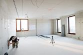Một người mặc thiết bị an toàn đang căn chỉnh các vạch kẻ trên tường bằng máy cân bằng laser trong một căn phòng sáng.